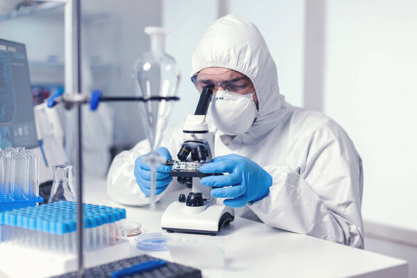 Ученый смотрит в микроскоп, одетый в костюм ppe