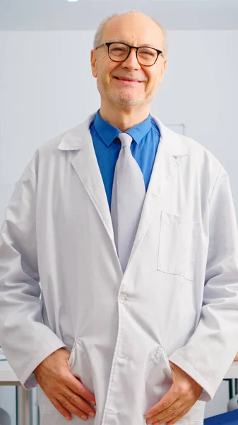 Retrato de homem idoso cirurgião em pé na frente da câmera sorrindo — Fotografia de Stock