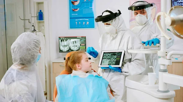 Tandläkare i skyddsutrustning visar på tablett tandröntgen granska det — Stockfoto