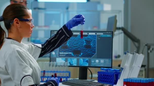 Científico médico mirando la muestra de sangre y la escritura en el ordenador — Vídeos de Stock
