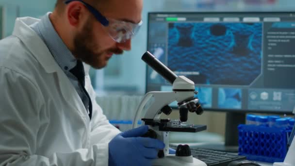 Científico masculino mirando bajo microscopio en laboratorio de desarrollo médico — Vídeo de stock