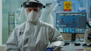 Laboratuvarda oturmuş kameraya bakan yorgun bir mikrobiyolog.