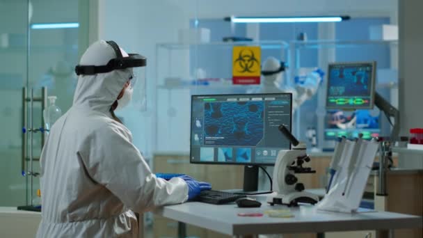 Медичний вчений в костюмі ppe, який працює з ДНК сканування зображення на pc — стокове відео