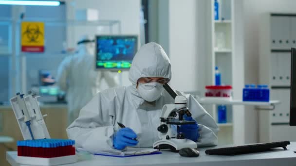 Medyczny naukowiec w skafandrze ppe przeprowadzający eksperymenty DNA pod mikroskopem — Wideo stockowe