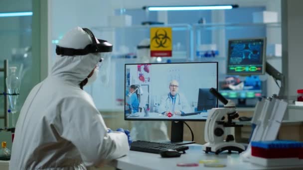 Chemist in ppe suit listening professional doctor on video call — Stock Video