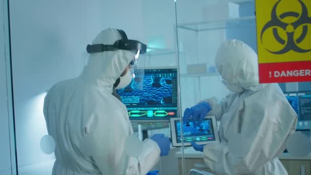 Ученые в покрывале, стоящие за стеклянной стеной, работающие в опасной зоне лаборатории — стоковое видео
