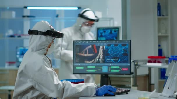 Biologo medico in tuta ppe controllare la digitazione del campione liquido sul pc — Video Stock