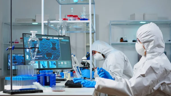 Cientista em terno ppe segurando tubo de teste com líquido azul em laboratório estéril — Fotografia de Stock