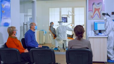 Koruma maskeli hastalar diş sağlığı kliniğinde doktor bekliyorlar.