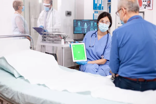 Медсестра в маске для лица держит планшет с зеленым экраном — стоковое фото