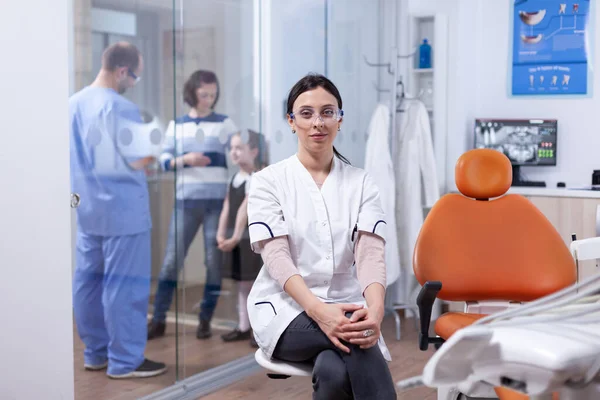 Стоматолог в стоматологическом кабинете сидит на стуле, пока ассистент разговаривает с пациентами — стоковое фото
