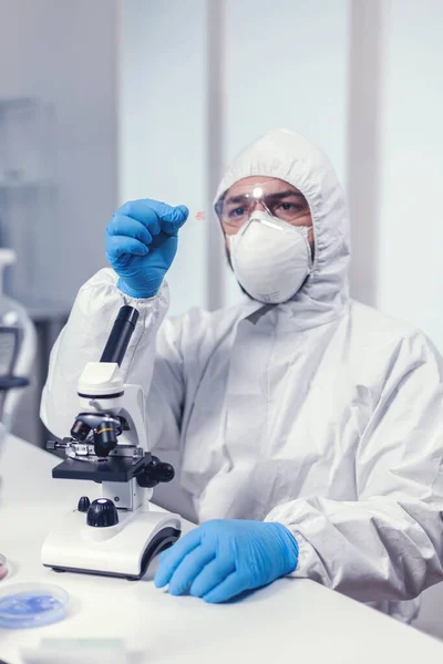 Микробиолог в костюме ppe анализирует образец на стеклянной ползунке микроскопа — стоковое фото