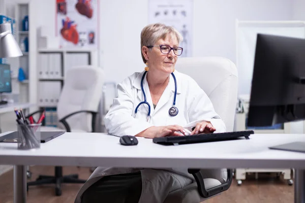 Лікар друкує на комп'ютері, сидячи в медичному кабінеті — стокове фото