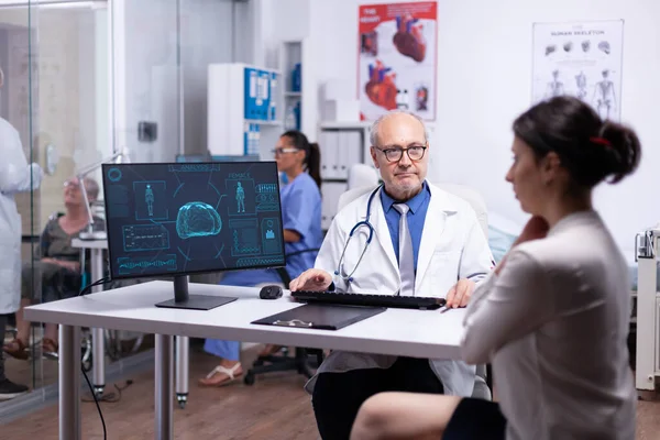 上了年纪的医生在电脑上向年轻女士解释身体扫描 — 图库照片