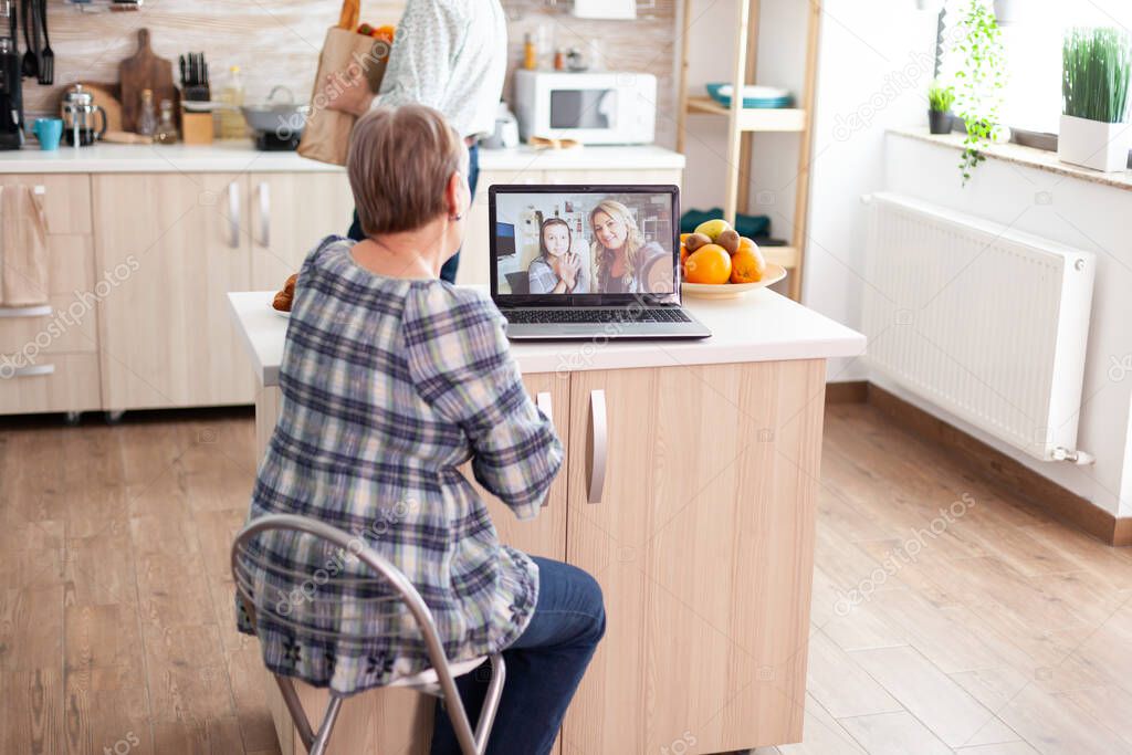 Enthusiastic senior woman talking with family online using laptop webcam