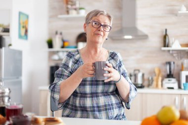 Mutfakta elinde bir fincan kahveyle kameraya bakan neşeli son sınıf öğrencisi.