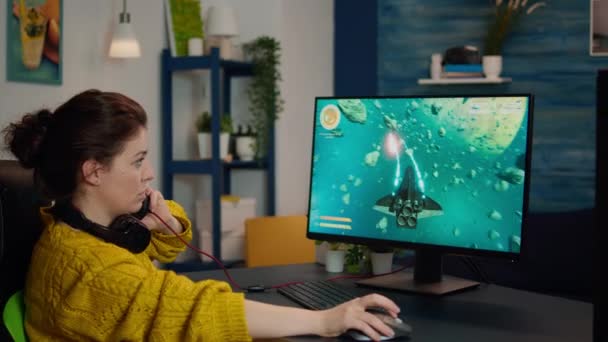 Εστιασμένη γυναίκα gamer κάθεται στο γραφείο, βάζοντας ακουστικά — Αρχείο Βίντεο