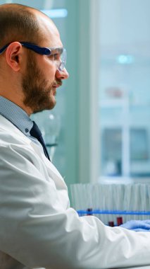 Laboratuvar önlüklü bilim adamı test tüpündeki kan örneğini analiz ediyor.