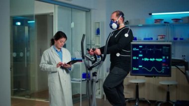 Spor bilimi laboratuvarında maskeli sporcu çapraz antrenörle koşuyor.