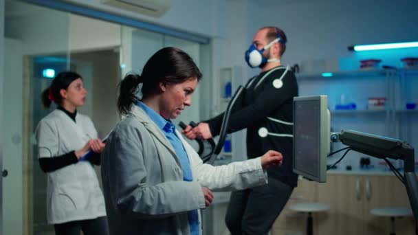 Lekarz sport naukowiec sprawdzanie EKG skanowania na monitorze, podczas gdy człowiek z maską działa — Wideo stockowe