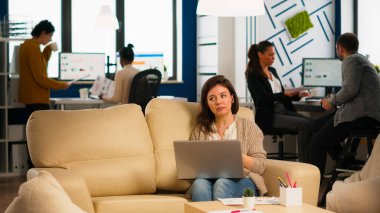 Yönetici kadın elinde dizüstü bilgisayarla kanepede oturuyor ve görüntülü konuşuyor.