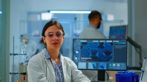 Chemist with lab coat sitting in laboratory looking at camera smiling