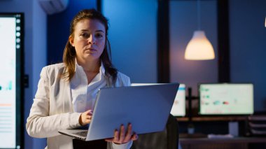 Yorgun yönetici başını kaldırıyor ve elinde dizüstü bilgisayarla kameraya bakıyor.