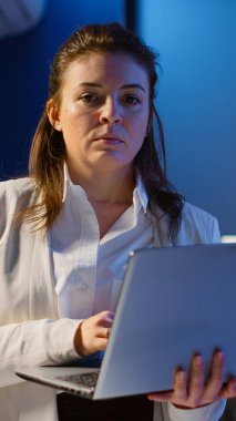 Yorgun yönetici başını kaldırıyor ve elinde dizüstü bilgisayarla kameraya bakıyor.