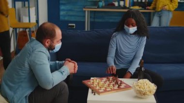 Elinde bira şişesi olan adam Afrikalı kadınla satranç oynuyor.