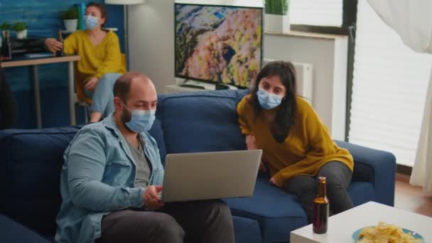 Мужчина в маске показывает новый фильм на ноутбуке женщине — стоковое видео