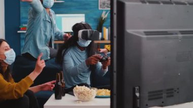 Yüz maskeli insanlar, video oyunu oynayan Afrikalı bir arkadaşı destekliyor.