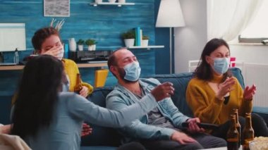 Bir grup çok ırklı arkadaş televizyonda komedi programı izleyip gülüyor.