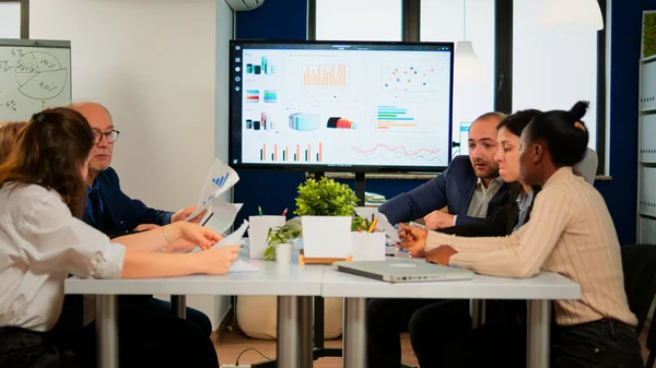 Man leader pointing at digital interactive whiteboard sitting at brainstorming table