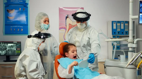 Little girl wearing ppe suit looking in the mirror after dental intervention