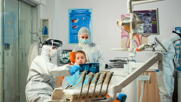 Pediatric dentist wearing protection suit treating girl patient