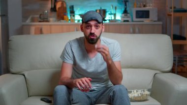 Göz maskeli konsantre bir adam televizyonun önünde oturuyor.