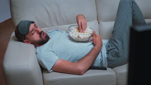 Hombre cansado relajándose en el sofá frente a la televisión comiendo palomitas de maíz mientras ve el programa de películas — Vídeos de Stock