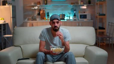 Televizyon karşısında oturan, uyku maskeli, konsantre bir adam.