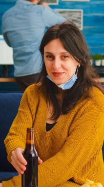 Maskeli genç bayan oturma odasında bira içiyor.