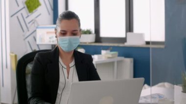 Koruyucu yüz maskeli bir iş kadını dizüstü bilgisayar pazarlama istatistiklerinde analiz yapıyor.