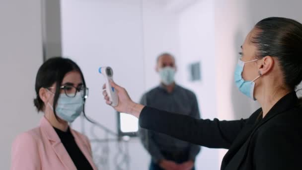 Yüzü maskeli bir iş kadını meslektaşlarının alnının sıcaklığını kontrol ediyor. — Stok video