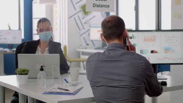 Homem de negócios usando máscara facial falando ao telefone enquanto sentado na mesa — Vídeo de Stock