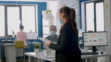 Koruyucu maskeli bir iş kadını takım sıcaklığını kontrol ediyor.