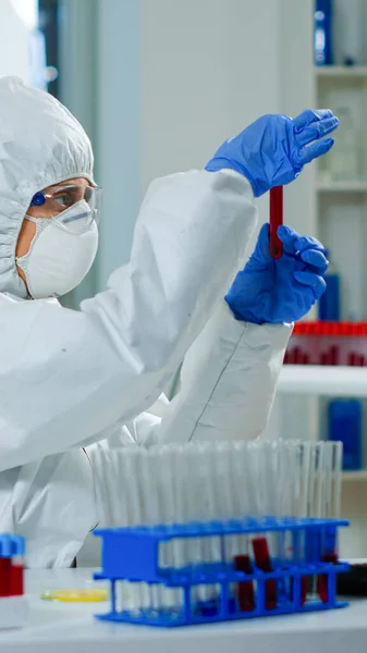 Researcher in coverall holding test tubes with blood sample