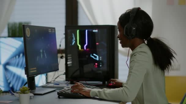 Spännande svart kvinna spelare sitter på skrivbordet, med headset med mick spela — Stockvideo