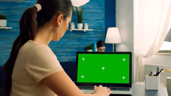 Woman typing on computer laptop with mock up green screen chroma key display