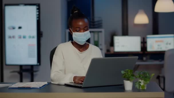 African woman with face mask reading emails late at night to respect deadline — Stock Video