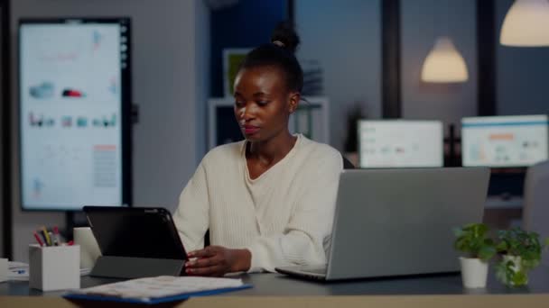 Mujer gerente africano utilizando el ordenador portátil y tableta en el mismo tiempo de trabajo horas extras — Vídeos de Stock