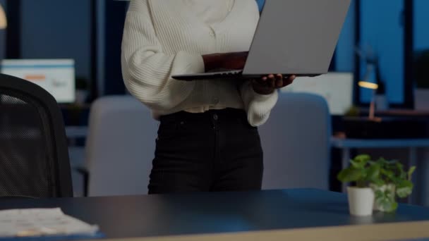 Африканский фрилансер смотрит на камеру улыбаясь держа ноутбук, стоящий возле стола — стоковое видео