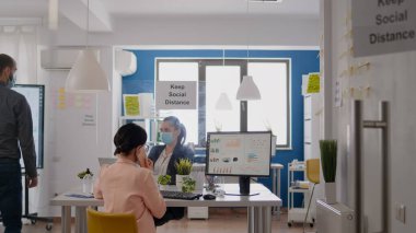 Tıbbi maskeli bir iş kadını ortaklarıyla akıllı telefondan konuşuyor.